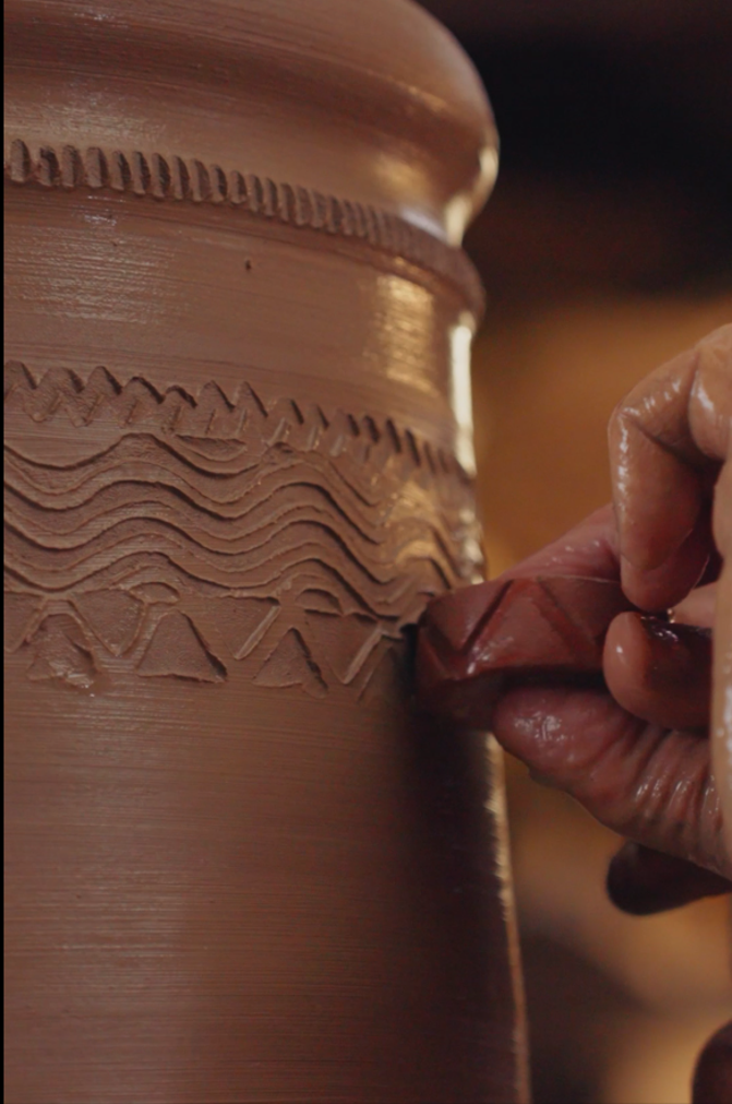 A close up of a roulette being applied to the top of a clay chimney pot before it's fired in the kiln.